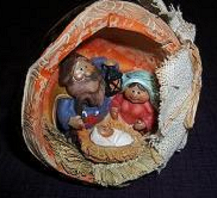 くるみの殻の中に作られた小さなキリスト降誕の場面。中央に藁の上で眠る幼子、左右にマリアとヨセフと思われる人形が寄り添って座り、素朴で温かい雰囲気。全体は茶色やベージュを基調に、手作り感のある質感が伝わる。